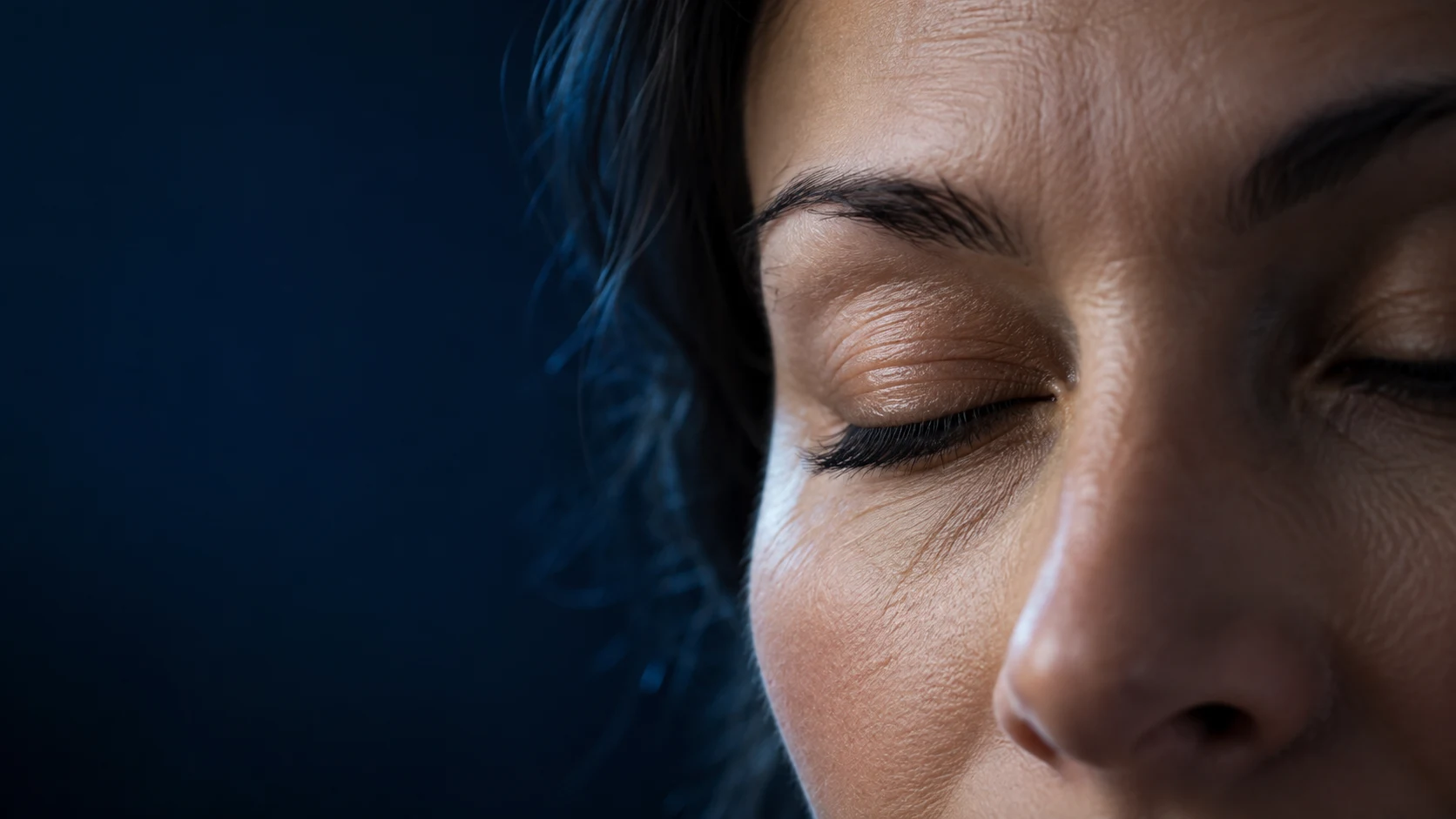 Close-up of an adult's eyelid gently closing over the eye during a blink, with realistic skin and eyelashes in subdued cinematic light