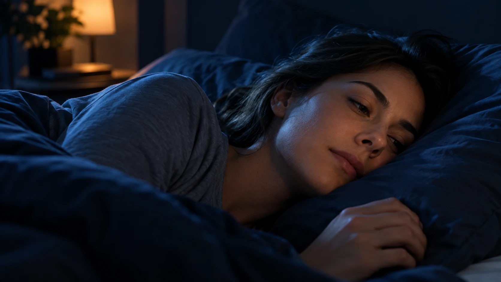 Woman resting on her side in a dark bedroom, breathing calmly with her face against a navy pillow