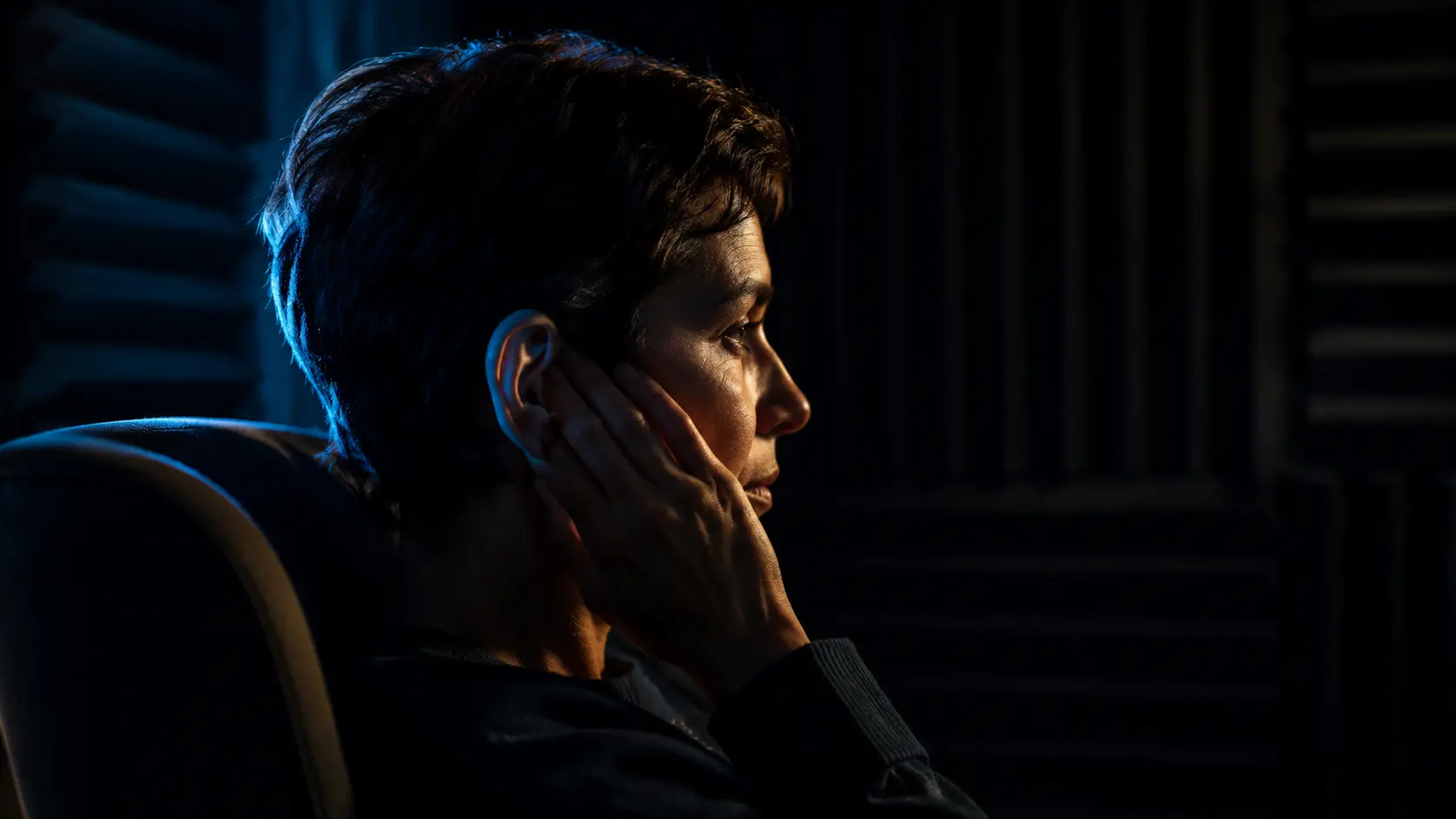 Adult listening in a quiet acoustic room with one hand resting lightly beside the ear